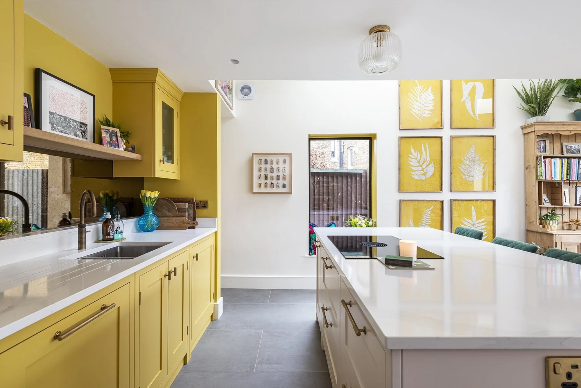 yellow kitchen with granite floors, white countertops and island bench, with brass taps, yellow artworks on the back wall