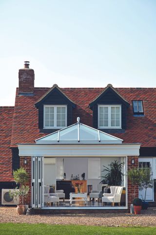 a glass and brick orangery attached to period property, with white armchairs and coffee table inside, by anglian home improvement