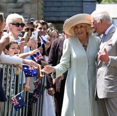 King Charles and Queen Camilla smiling and greeting a crowd of Australian fans outside a church