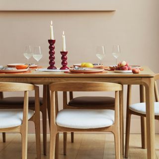 A light wood dining table with matching dining chairs decorated with two lit candlestick of various heights