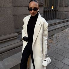 @ingridedvinsen carries a cream top-handle bag whilst wearing a cream coat over a black outfit