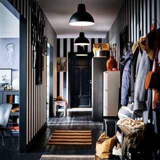 A hallway with black and white striped wallpaper, black flooring and black pendant lights