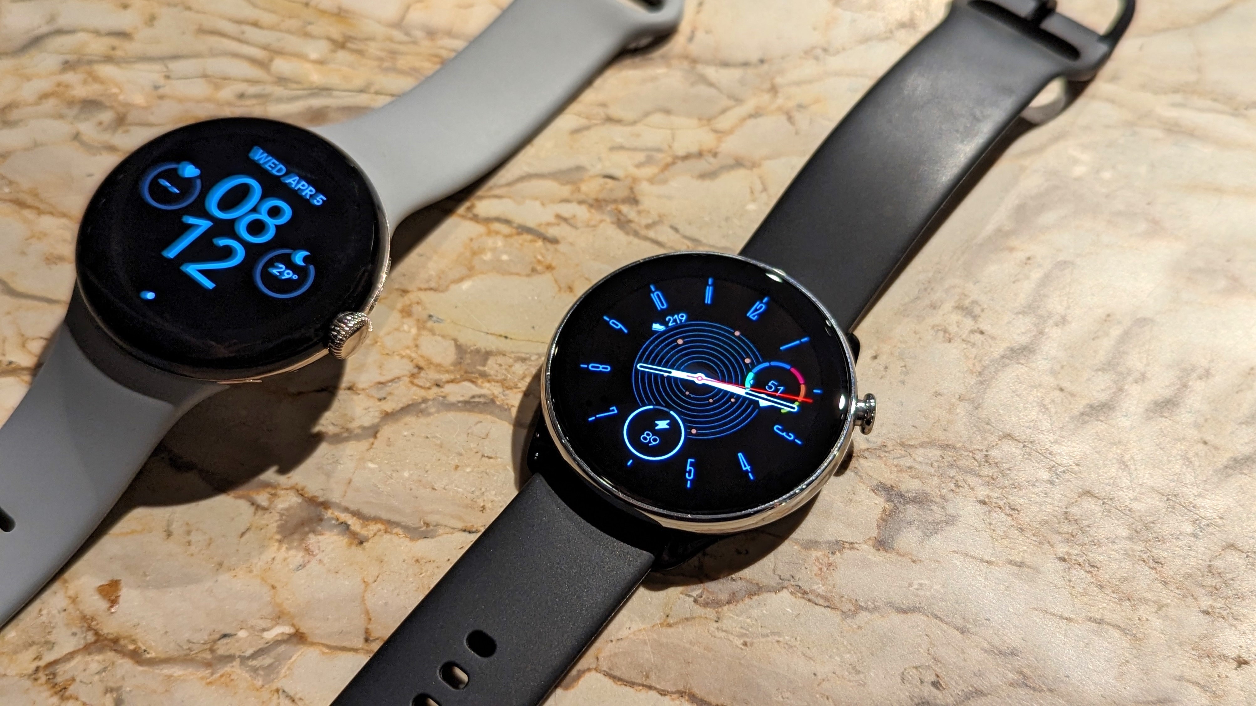 Relógios inteligentes Google Pixel Watch e Amazfit GTR Mini mantidos sobre uma mesa de mármore.