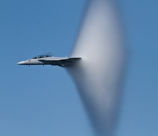 A vapor cone forming around an F-18 approaching Mach 1.