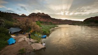 A group of people camp after rafting on the Colorado River at sunset