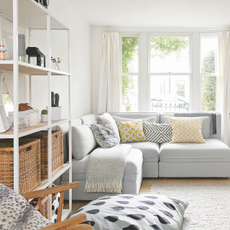 Airy living room with grey sofa, fire place and shelving unit with woven storage boxes.