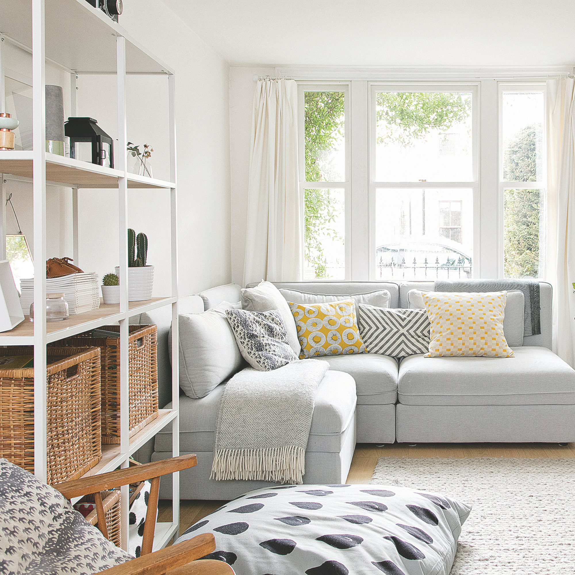 Airy living room with grey sofa, fire place and shelving unit with woven storage boxes.
