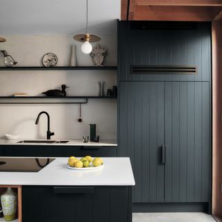 Dark wood panelled kitchen cabinets with white worktops, open shelving and kitchen island