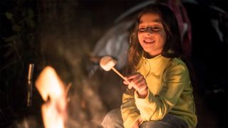 Young girl toasting marshmallow over camp fire
