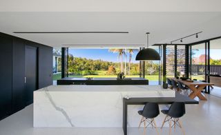 The central kitchen islands are made of white marble look porcelain and matte black laminate, creating a balanced alley of space within the open plan design