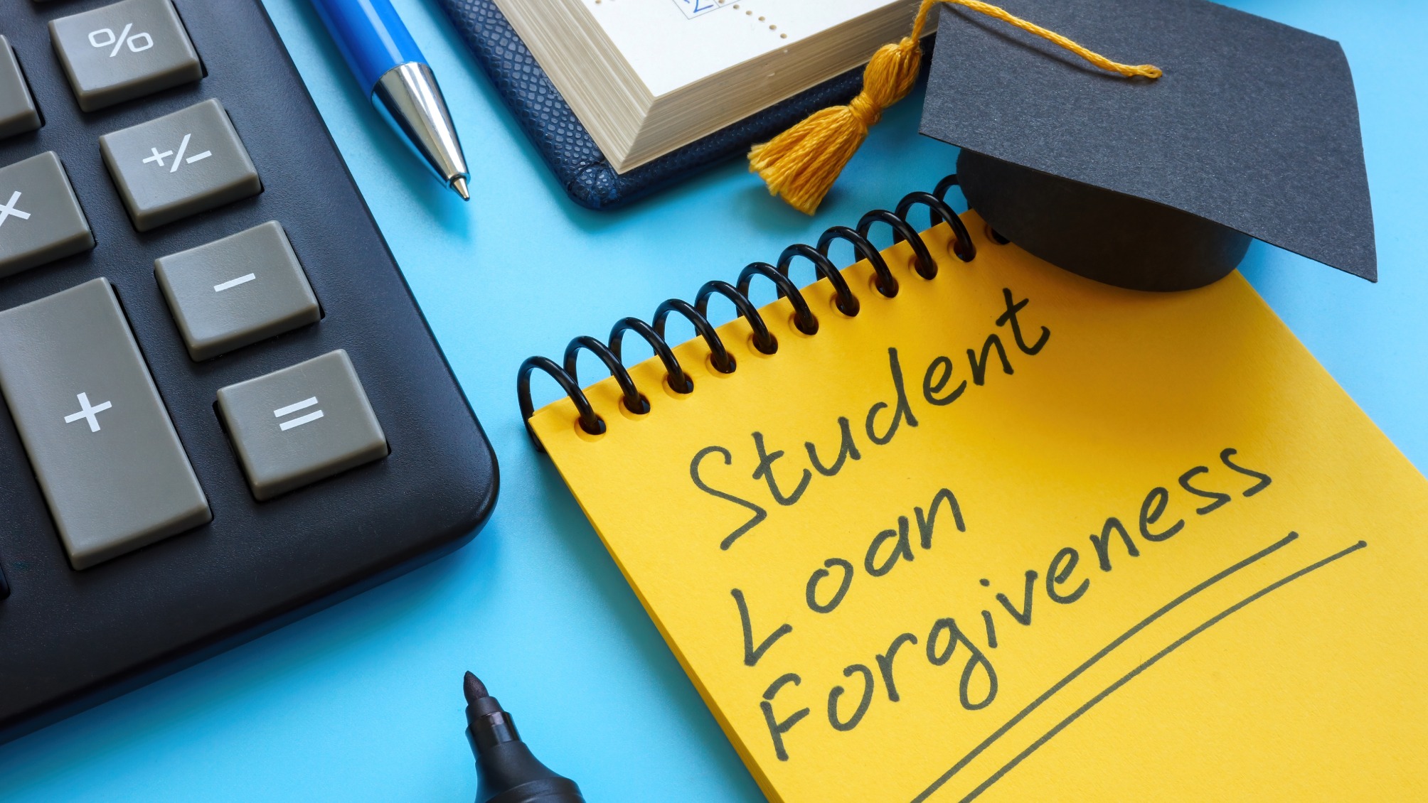 Close up of a yellow notepad with student loan forgiveness written on it in marker pen