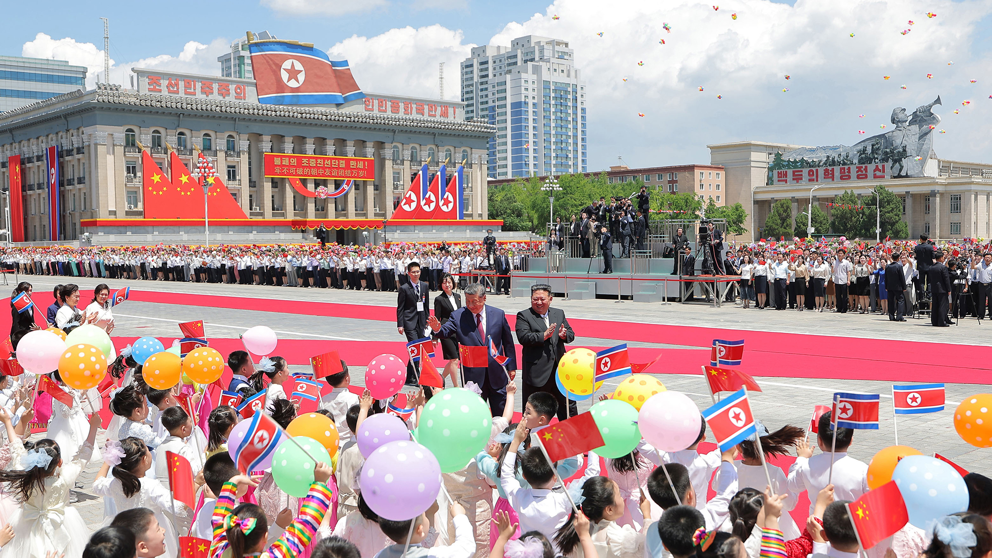 Chinese President Xi Jinping and North Korean leader Kim Jong Un greet children waving flags during a welcome ceremony in Pyongyang, North Korea