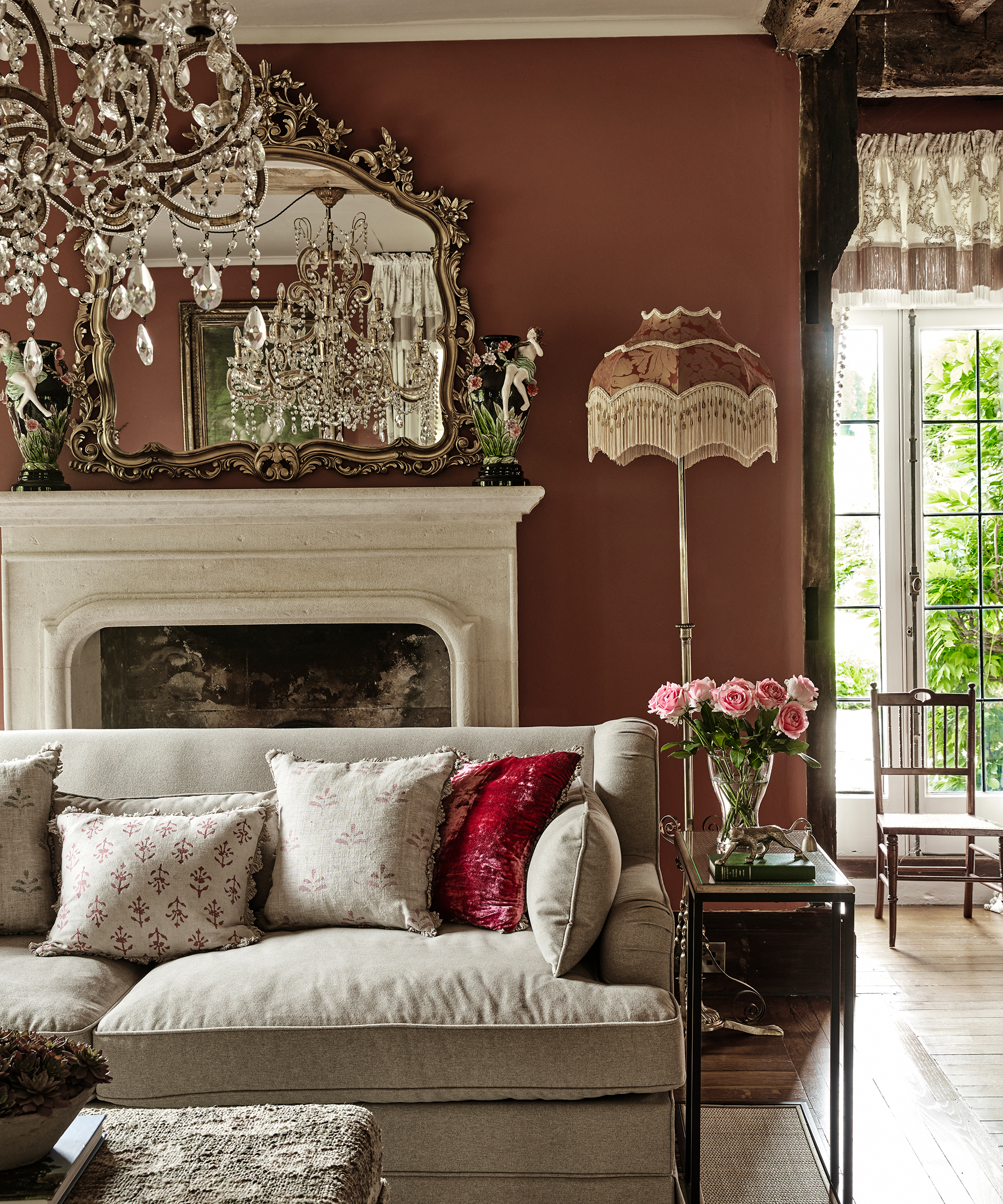 Elegant living room with earthy red walls, crystal chandelier, neutral sofa and marble fireplace