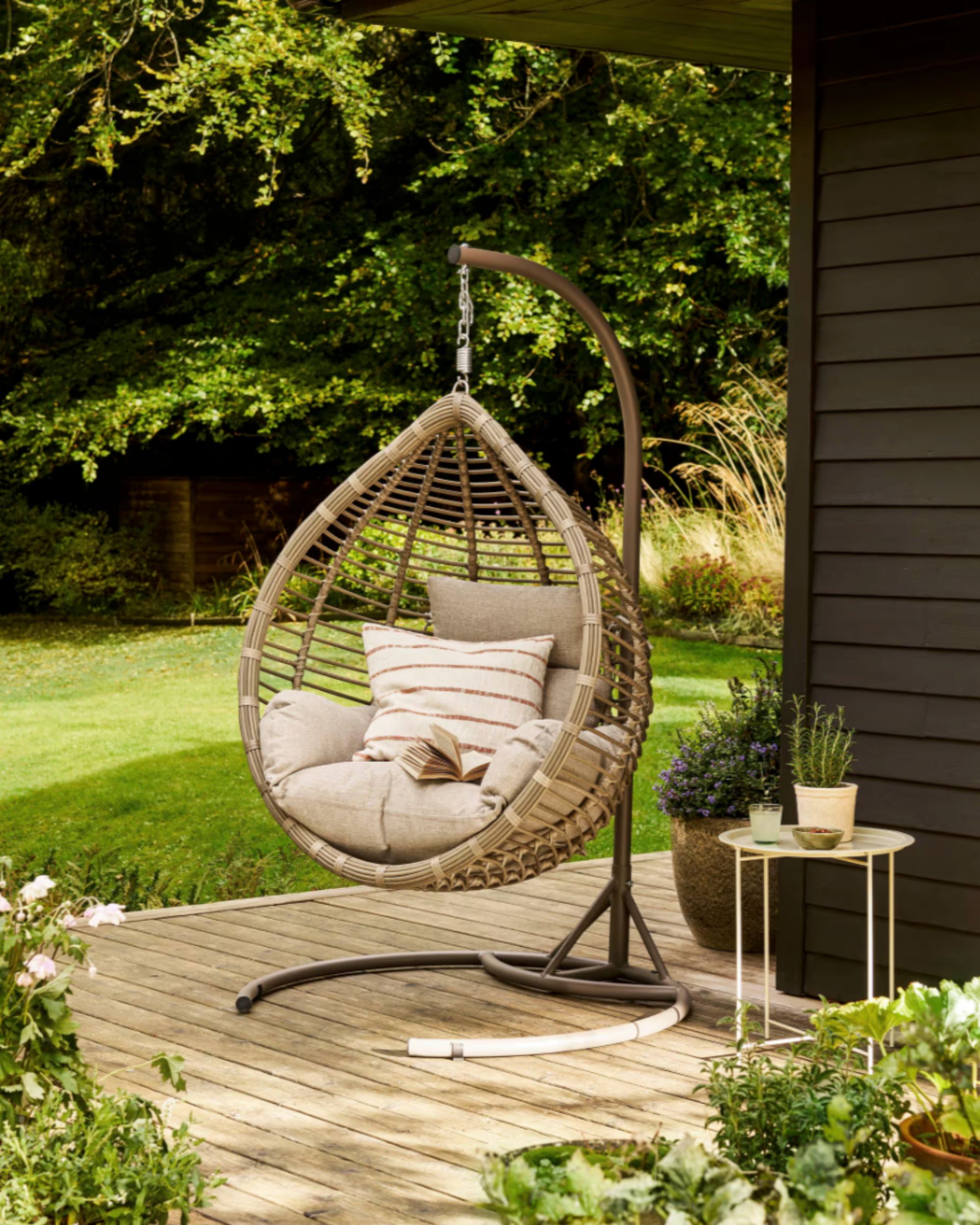 a hanging woven egg chair on decking with neutral seat cushions