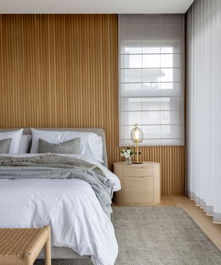 Bedroom with fluted cladded wall, bed, bedside table.