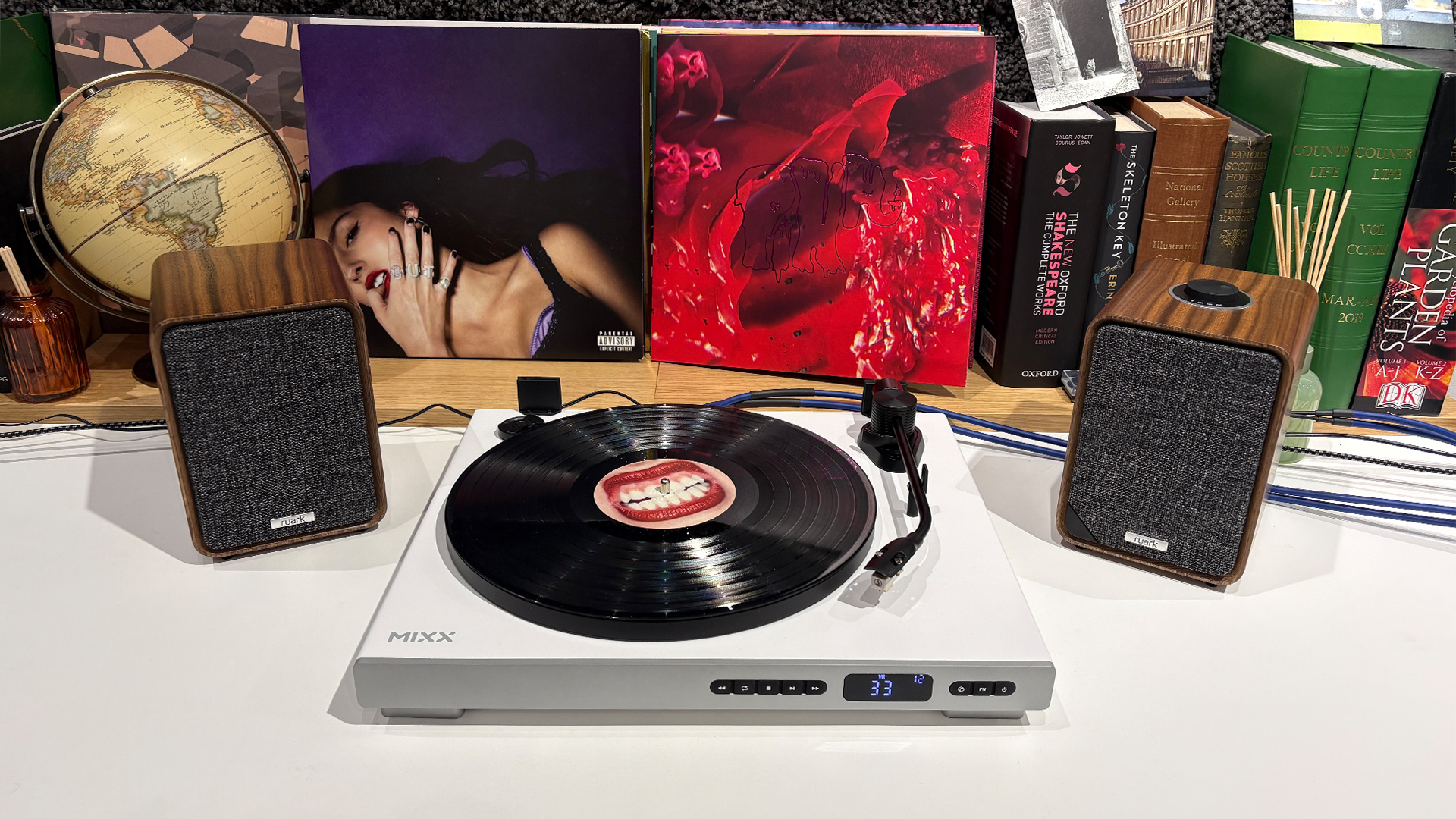 Mixx Analog+ turntable/CD player on white surface in front of busy shelf flanked by Ruark MR1 Mk3 desktop speakers