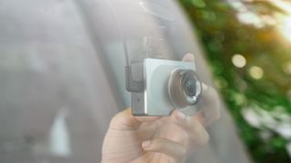 A hand positioning a dash cam inside a car windscreen