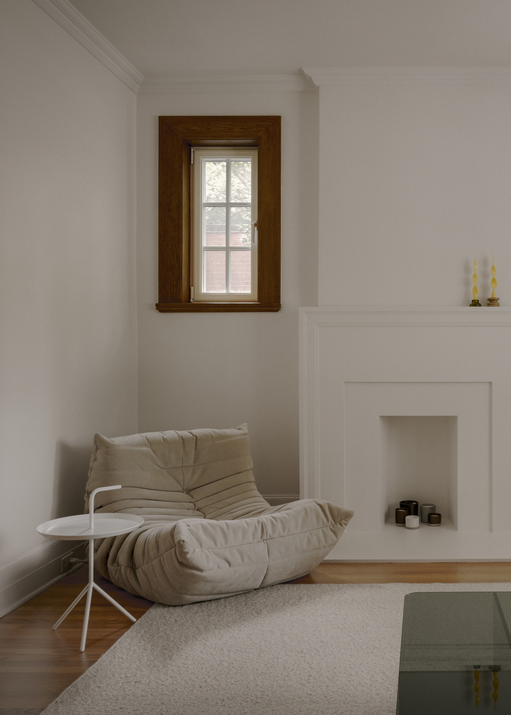 A minimalist nook with a Togo chair, a white side table and a fuzzy rug by a fireplace with candles