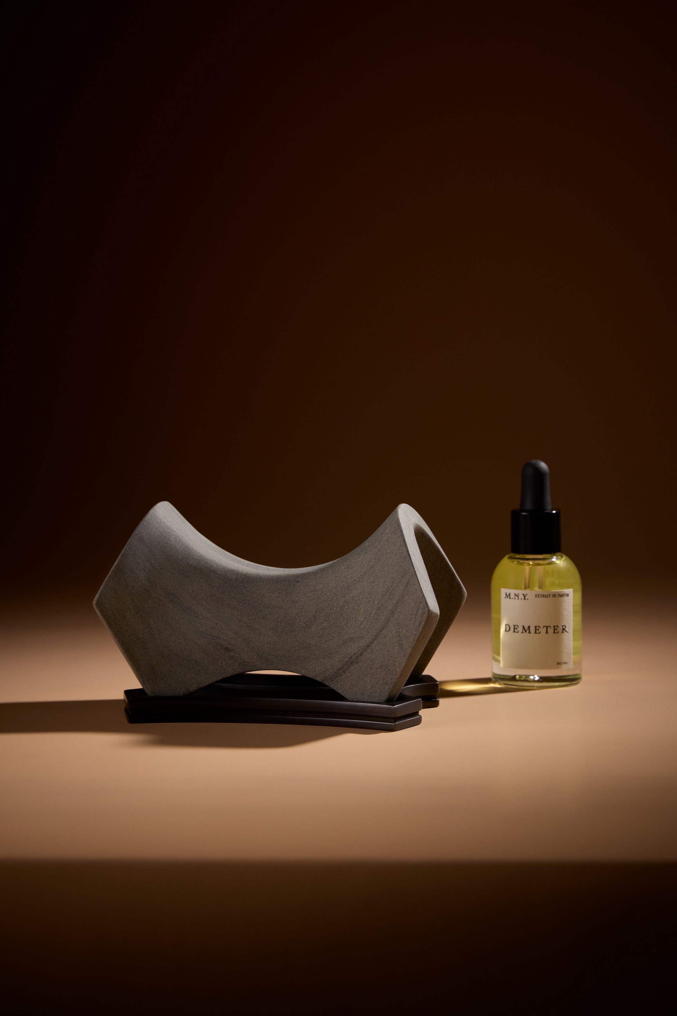 A product shot of a new stone diffuser with a saddle-like shape, alongside a vile of the fragrance oil.