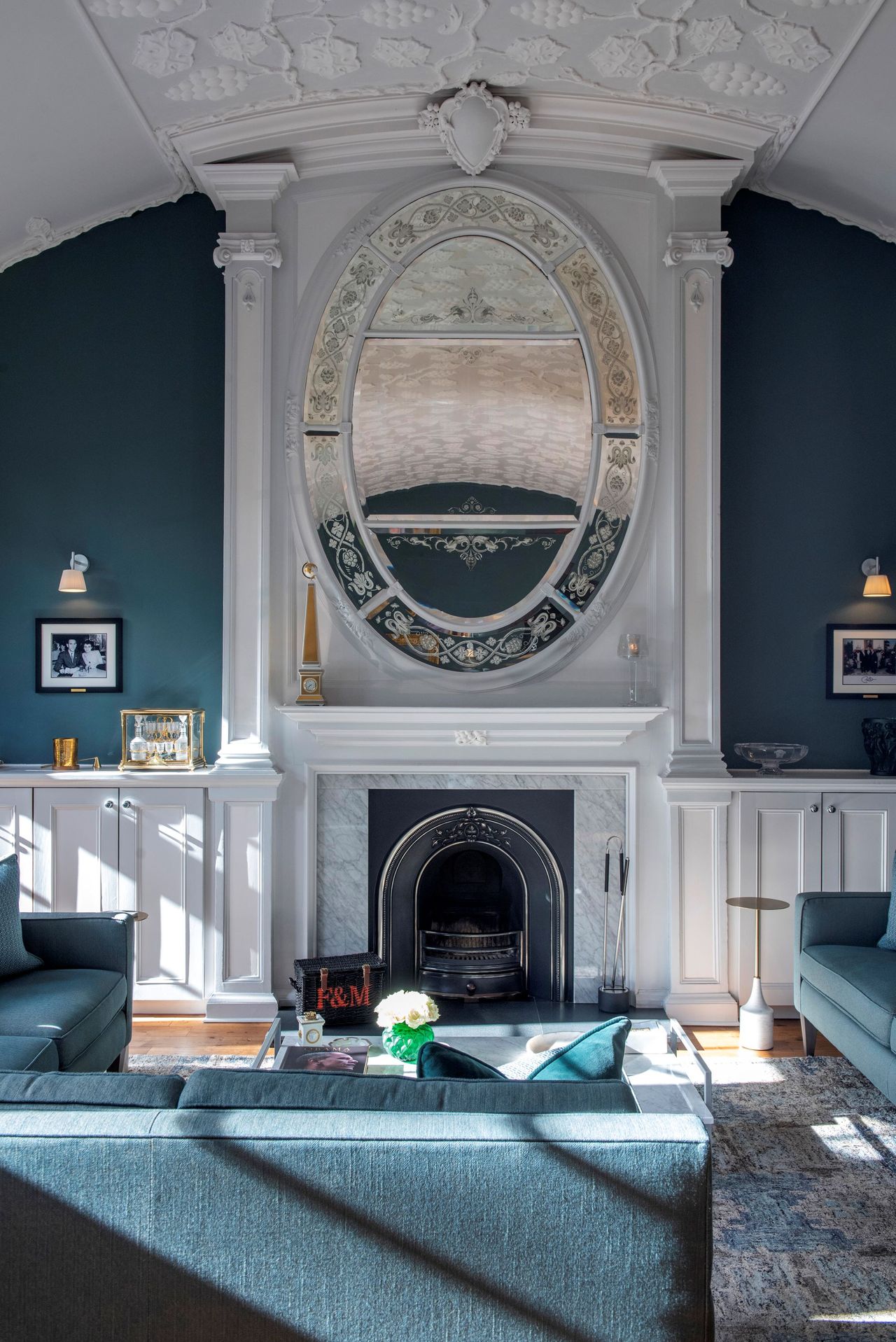 The living room includes a black fireplace which has a large mirror above with 3 green sofas facing the fireplace