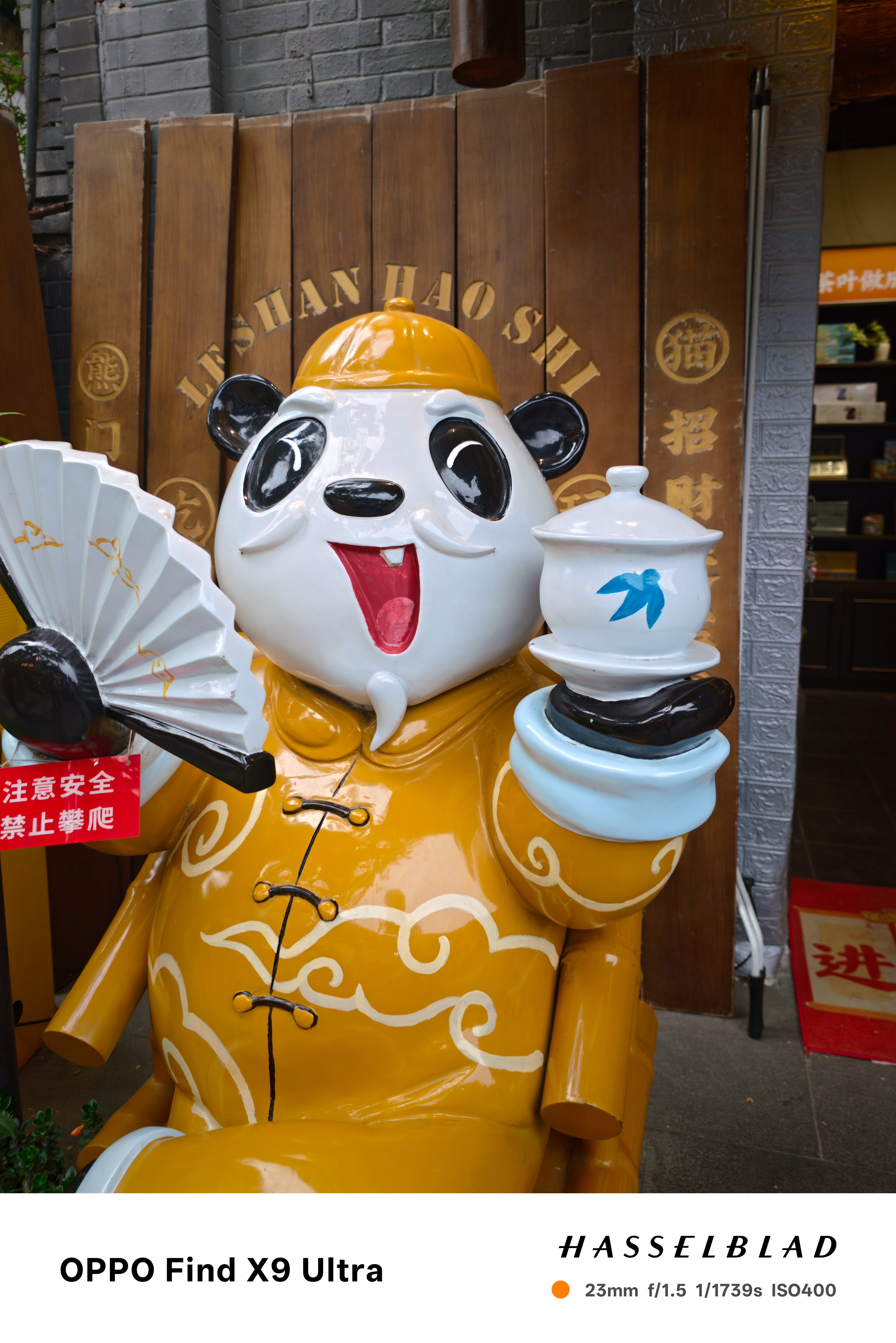 Panda statue holding a fan and teacup outside a shop entrance
