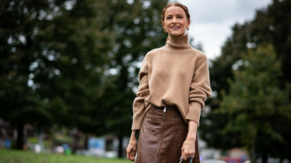 A guest attends milan fashion week spring summer 2025 in beige turtleneck sweater and brown leather skirt smiling 