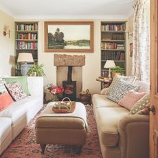 A narrow living room with two sofas facing each other, bookcases built into alcoves and a wood burning stove in between