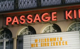 Exterior view of Yorck Kino Passage cinema featuring arched windows, a white sign board with yellow letters and red neon lights