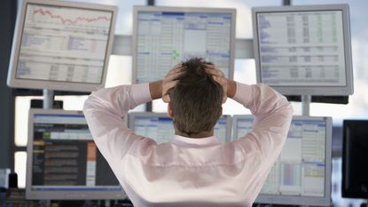 A man looking at multiple screens of investing returns puts his hands on his head in dismay.