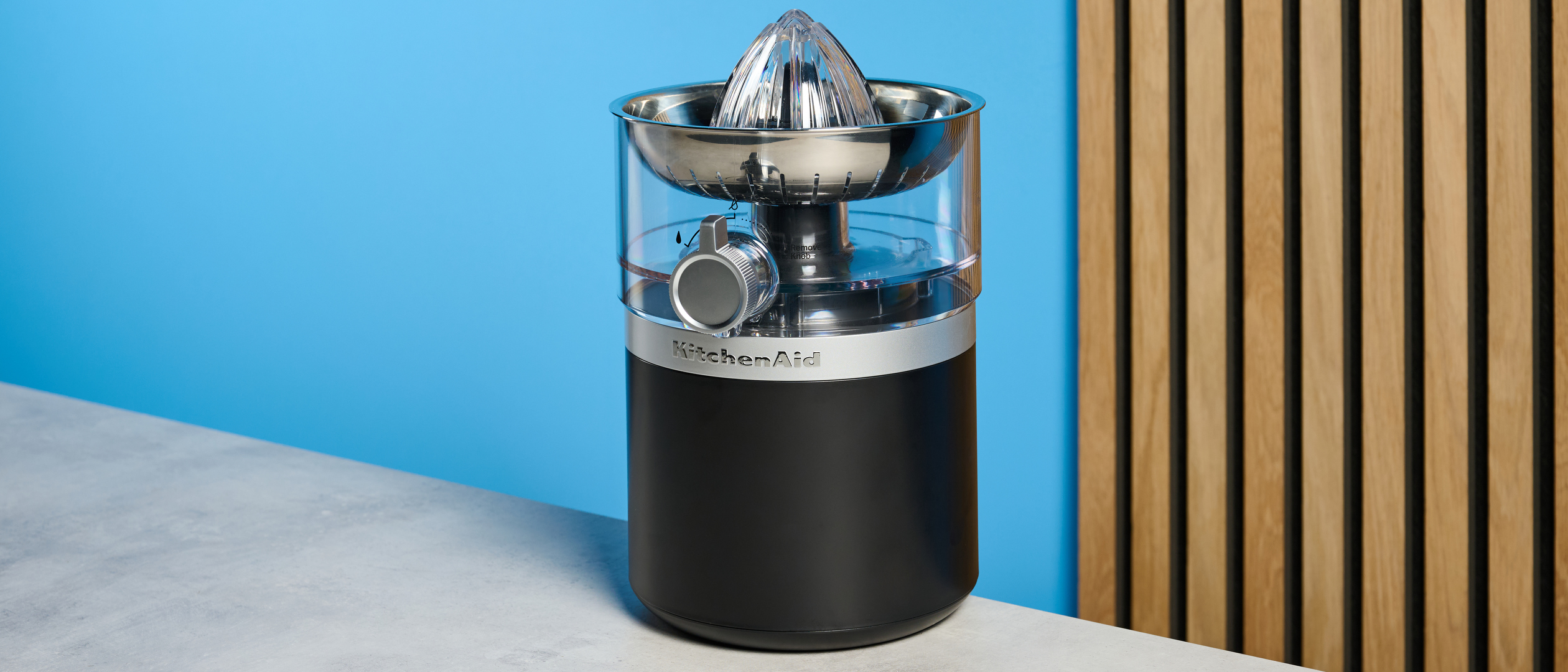 KitchenAid Go Cordless Citrus Juicer in matte black photographed in front of a blue background.