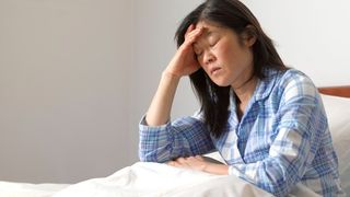 An asian woman holds her head with one hand, eyes closed and looks like she is in pain.