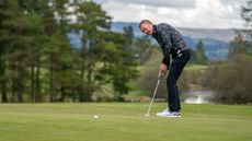 Fergus Bisset hits a putt on a golf course with trees in the background