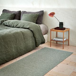 A bedroom with a low bed covered in dark green linen bed linen with a matching rug on the floor