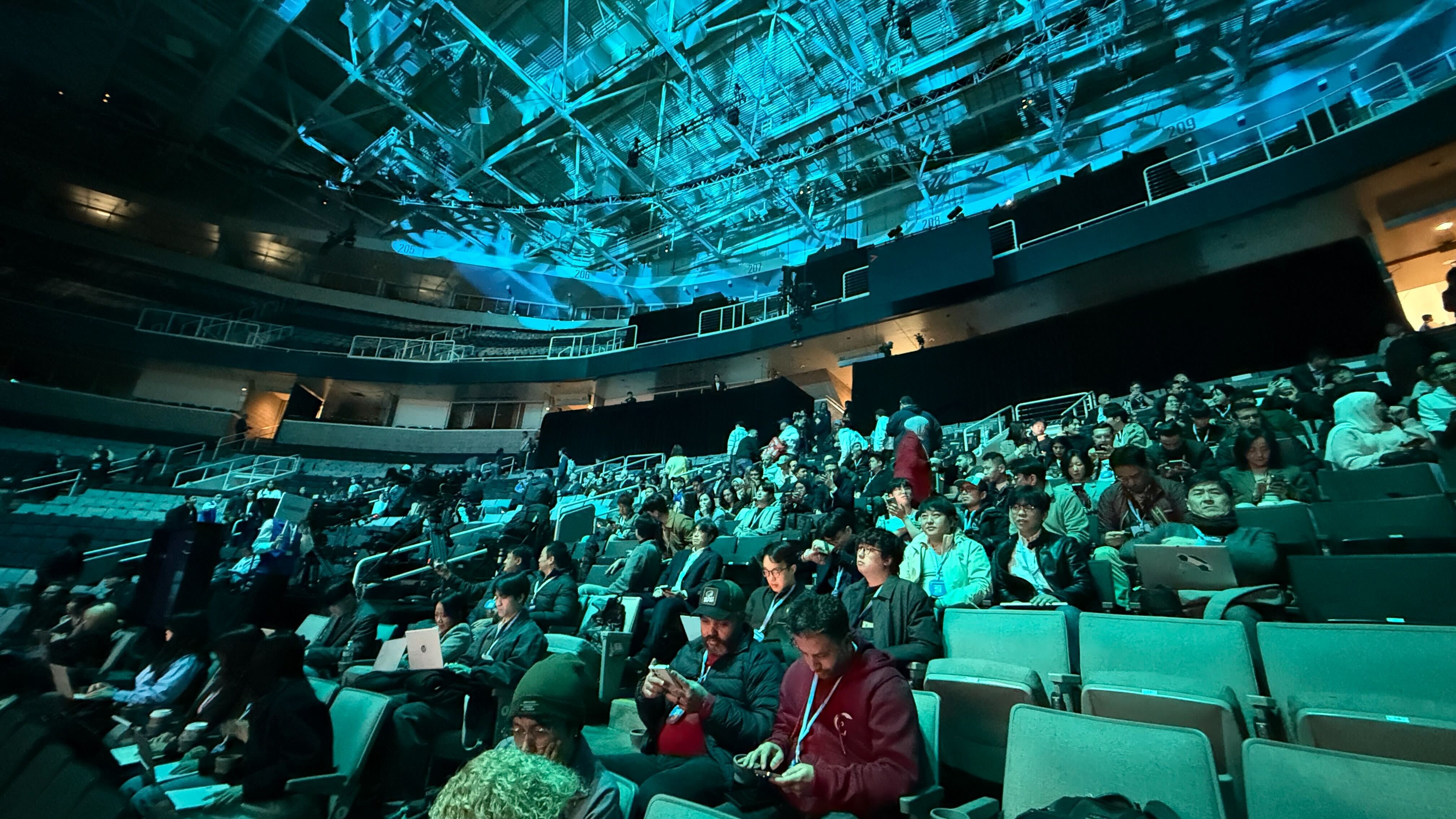 People in the auditorium at Galaxy Unpacked waiting for the show to begin, with dramatic blue lighting