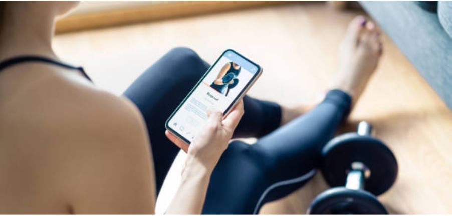 Woman sitting on the floor with a workout app on her phone and a set of dumbbells