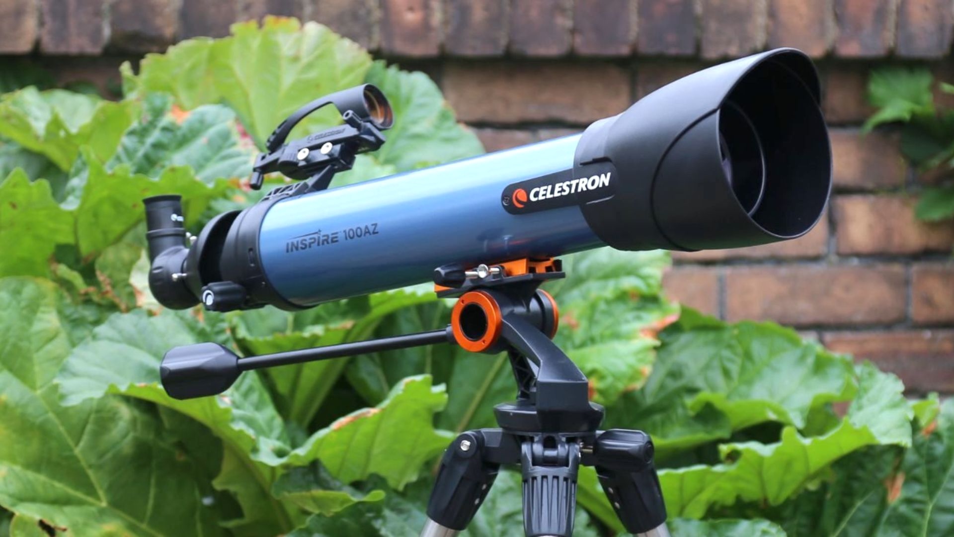 A Celestron telescope on a tripod in front of a bush.