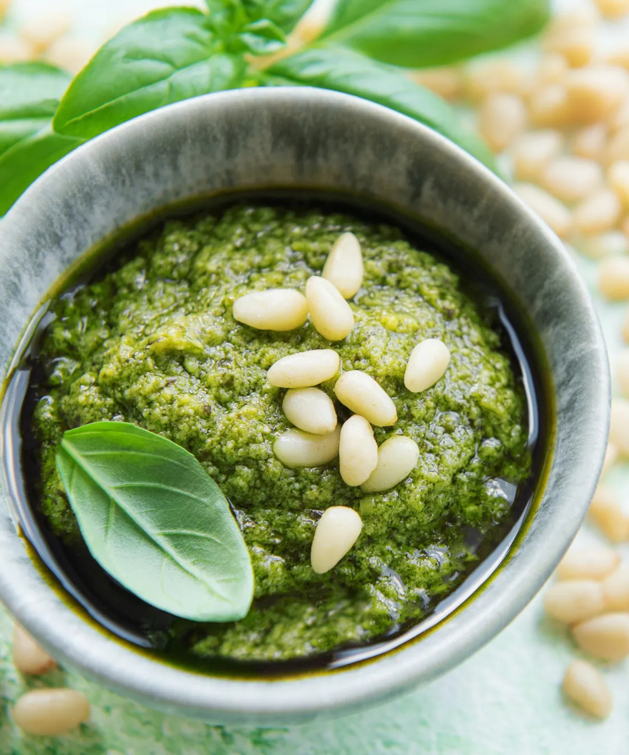 A pot of green teso with pine nuts, garlic and basil scattered on a table behind