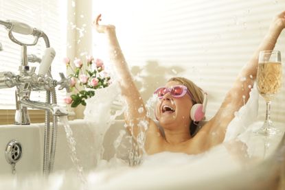 Woman wearing headphones splashing in bath