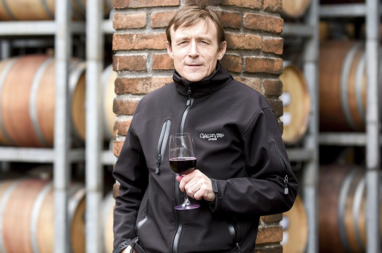 A man stands in a winery holding a glass of wine
