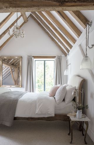 bedroom with white walls with beams and double bed with white headboard and chandelier