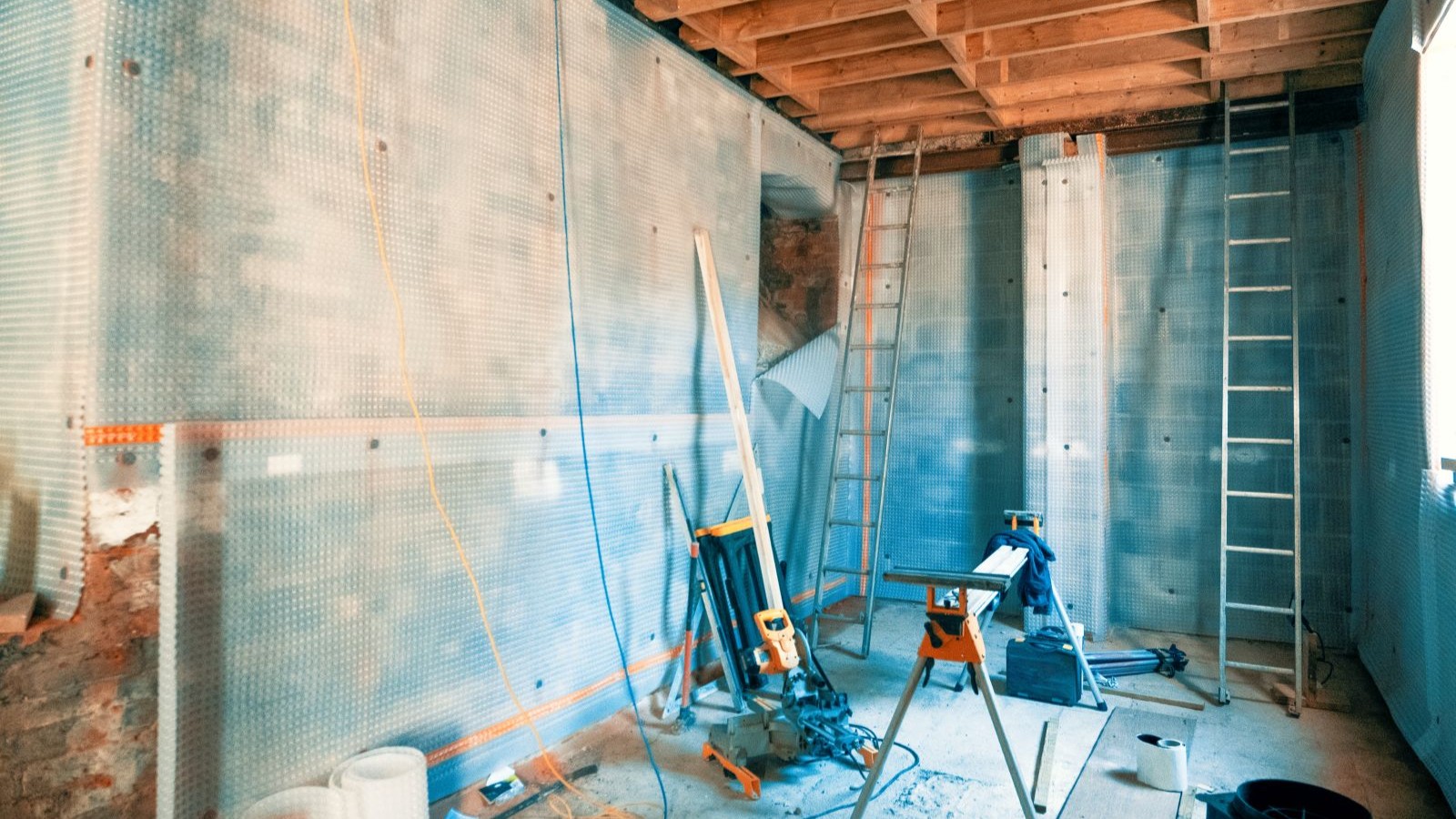 A basement being renovated with a ladder and tanking on the walls