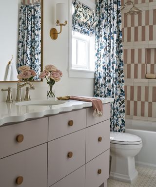 narrow bathroom with vanity, toilet and tub with patterned shower curtain and roman blind