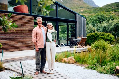 Mature man and senior woman with arms around each other, smiling towards camera, on vacation