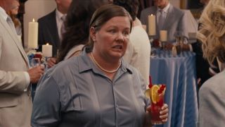 Melissa McCarthy holding a drink and cringing in Bridesmaids.