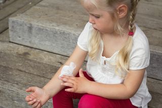 A little girl spreads lotion over her arm