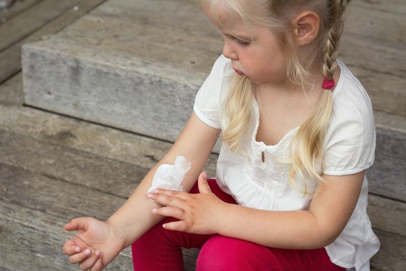 A little girl spreads lotion over her arm