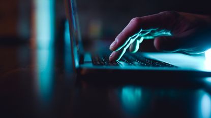 close up of a hand typing on a laptop keyboard in the dark