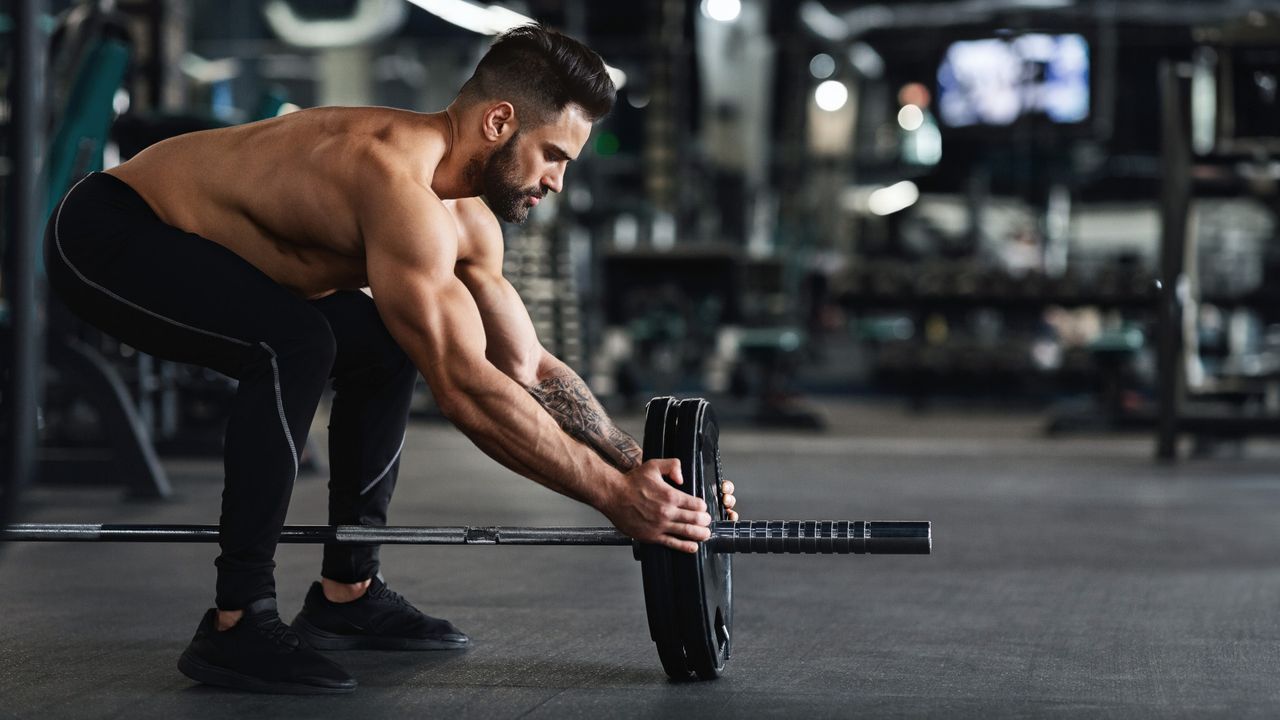 A man loading weight plates onto a barbell to perform meadow rows