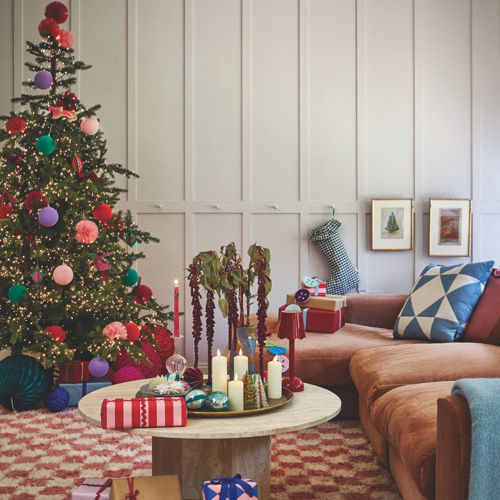 Christmas tree with colourful pom poms, paper decor and presents on a red checkerboard rug.