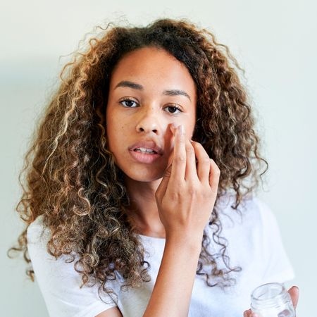 woman with eczema on her face applying cream